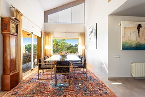 A spacious room with a large dining table, patterned carpet, and a view of greenery outside.