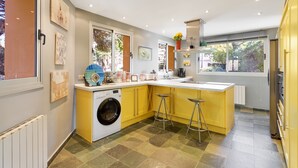 Una cocina moderna con lavadora incorporada, una isla grande con taburetes y vistas al jardín a través de la ventana.