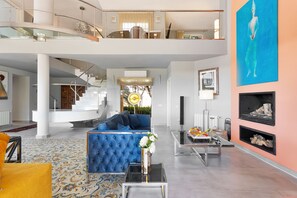 Amplia sala de estar con un sofá azul, una mesa de centro y un jarrón decorativo. Una escalera conduce a un nivel superior.