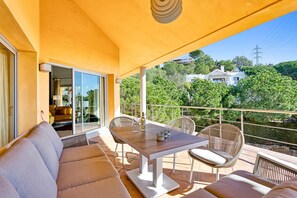 Eine sonnendurchflutete Terrasse mit Esstisch, Stühlen und einer Couch.