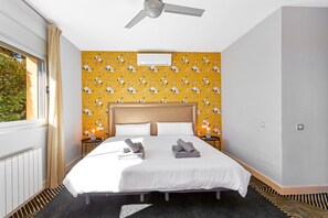 Ein Hotelzimmer mit einem Bett, einem Deckenventilator, einem Fenster mit Vorhängen sowie einer Wand mit ornamentalem Wandpapier.