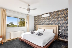 Ein Hotelzimmer mit einem großen Bett, einem Deckenventilator, einem Fenster mit Vorhängen und einem gemusterten Wandteppich.