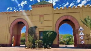 A building with two large arched entrances, a paved courtyard, and a clear blue sky.