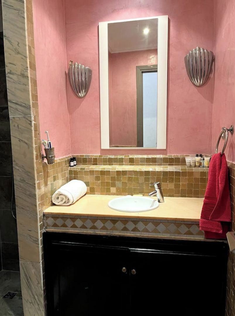 A bathroom with a pink wall, a white sink, and a mirror.