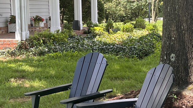 Deux fauteuils Adirondack sont placés dans un espace herbeux, avec un gazebo blanc et un arbre en arrière-plan.