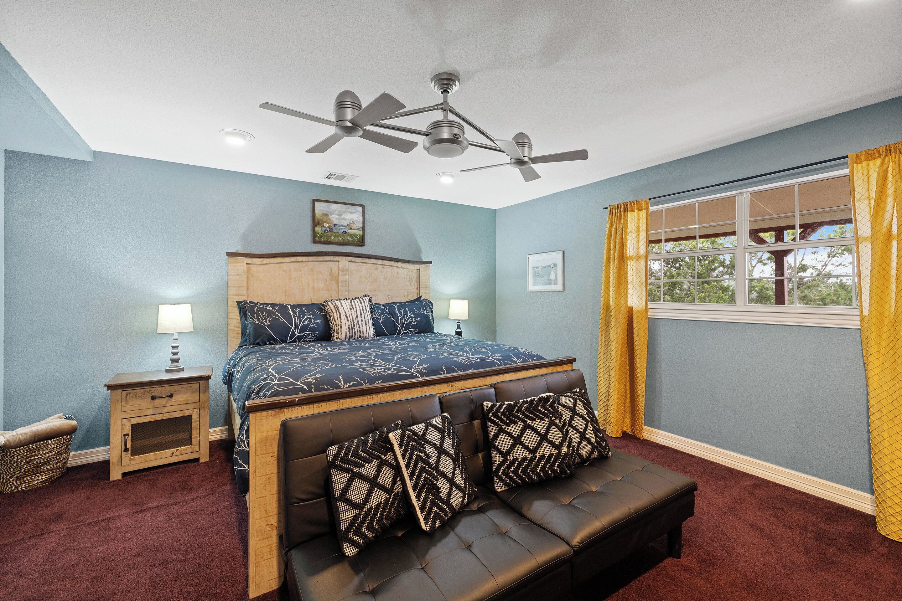 A bedroom with a bed, a bench, a nightstand, a ceiling fan, and a window with curtains.