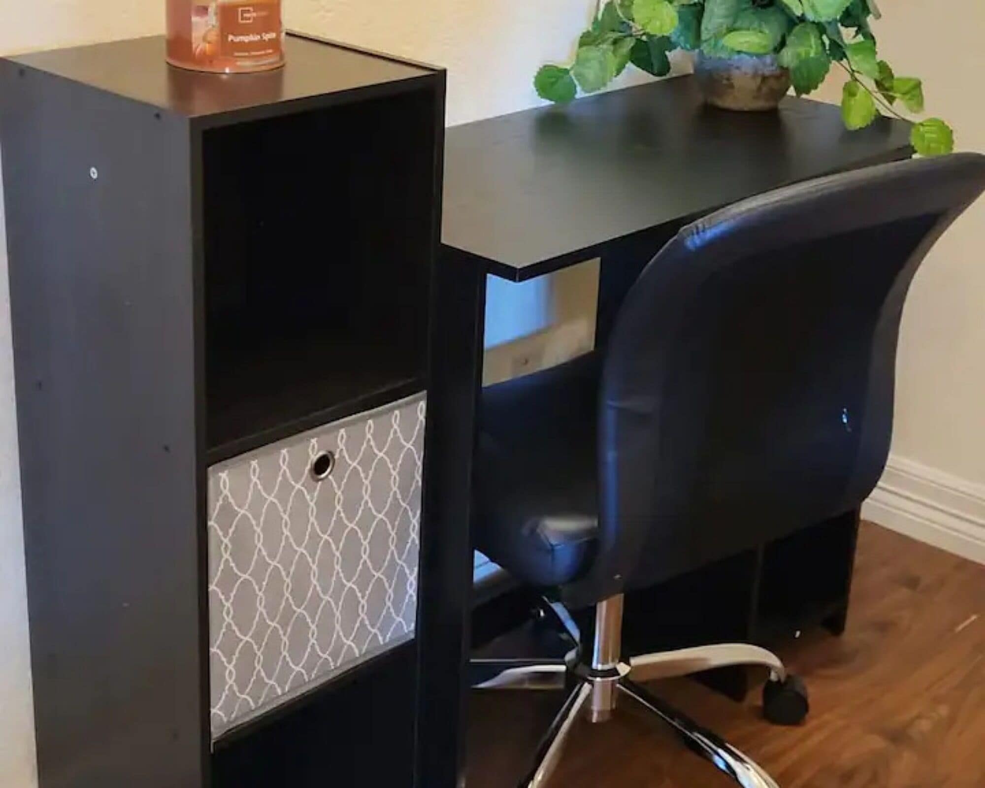 A black desk with a chair, a potted plant, and a pumpkin spice container.