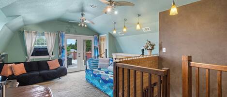 A spacious living area with a ceiling fan, a wooden bench, a sofa, and a colorful bedspread.