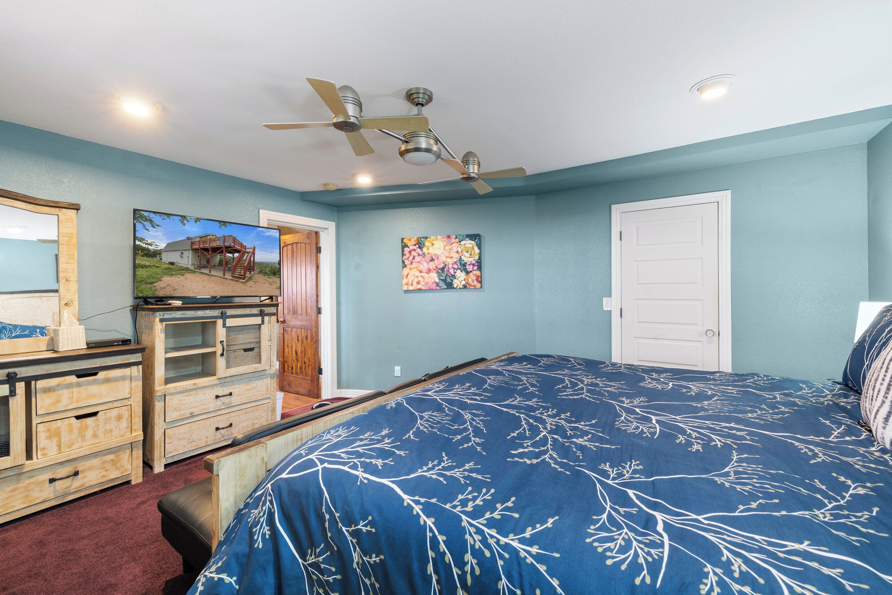 Une chambre à coucher avec un lit, une commode, un ventilateur de plafond et des œuvres d’art accrochées au mur.
