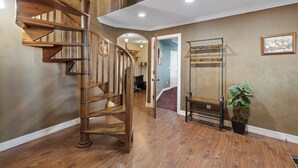 A wooden spiral staircase in a hallway with a potted plant and a metal rack.