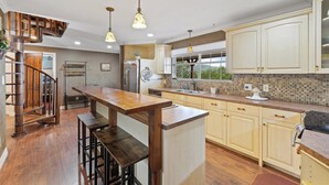A kitchen with wooden bar stools, a built-in island, and a view of the outdoors through a window.