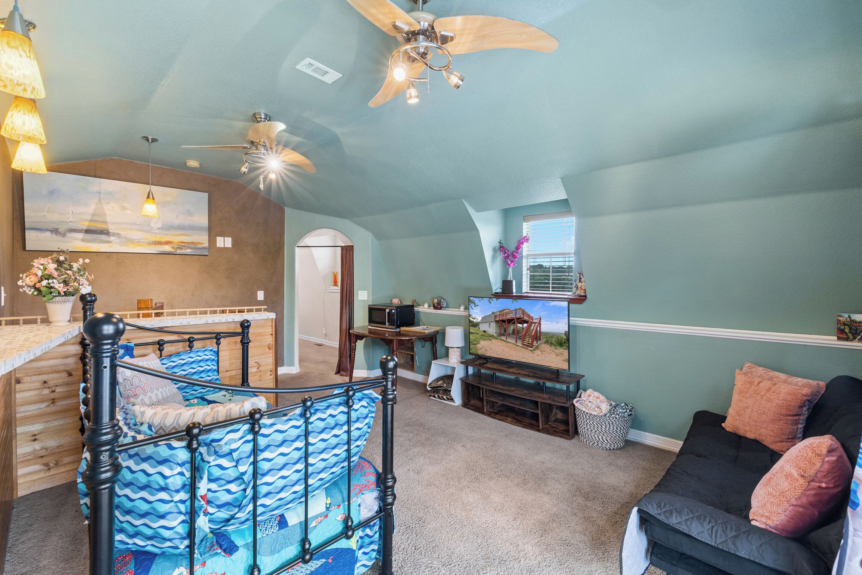 A spacious living area with a bed, a couch, a television, and a ceiling fan.