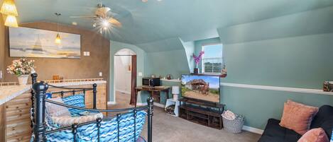 A spacious living area with a bed, a couch, a television, and a ceiling fan.