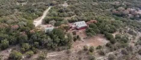Vista aérea de una propiedad rodeada de vegetación densa, con un camino que lleva a un edificio.