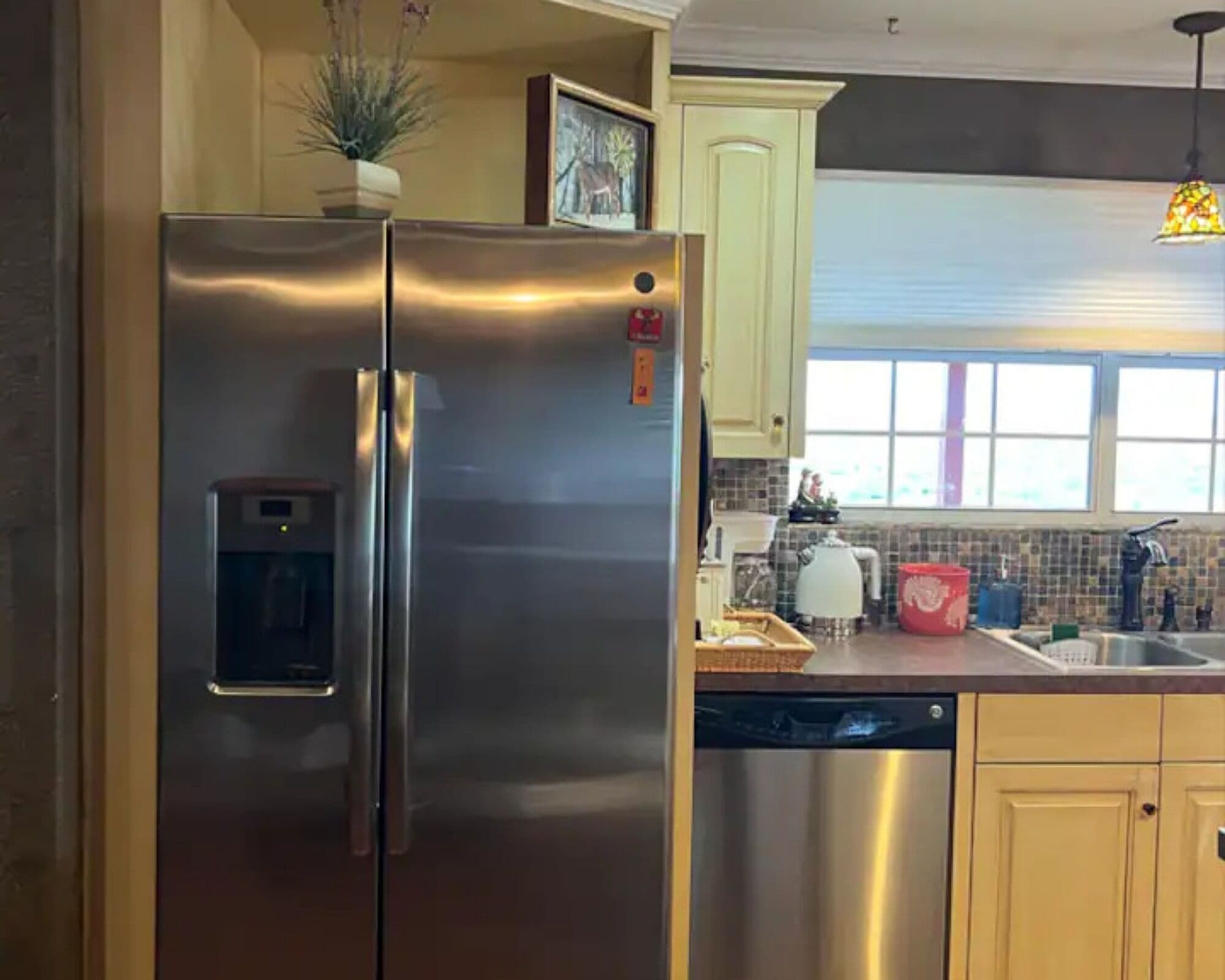 A stainless steel refrigerator with a water dispenser, a dishwasher, and a window above the sink.