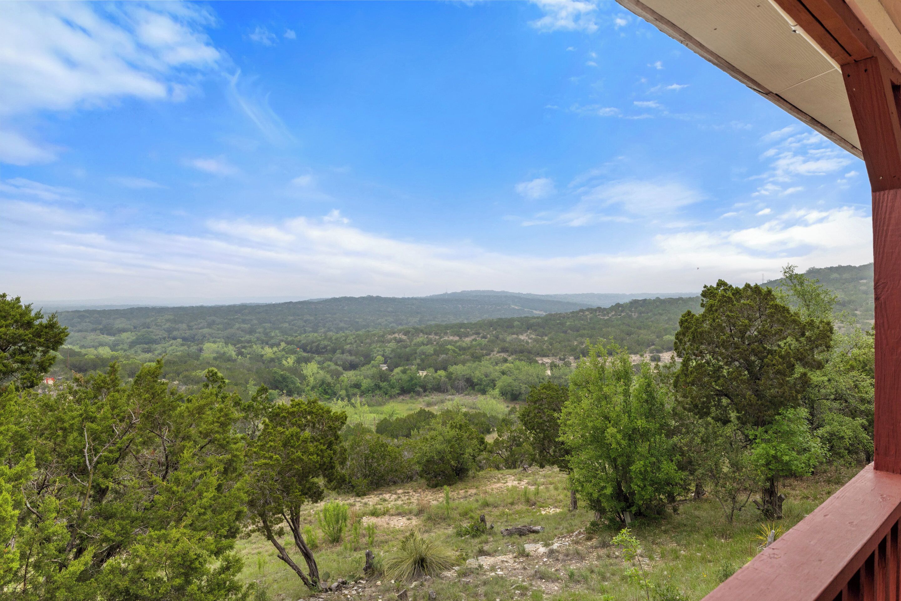 Vista desde un balcón sobre un paisaje exuberante con árboles y colinas lejanas bajo un cielo despejado.