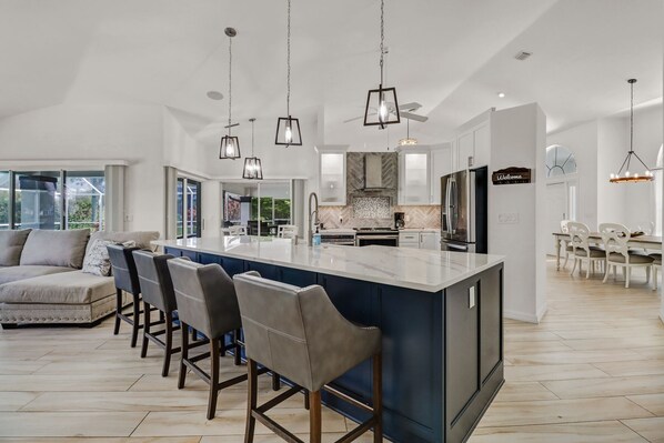 A modern kitchen with a central island, bar stools, and pendant lighting.