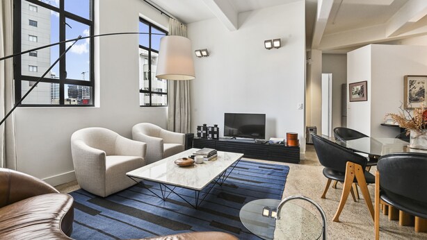 Uma sala de estar moderna com uma janela ampla, uma televisão de tela plana e uma área de refeições com uma mesa de vidro e cadeiras.