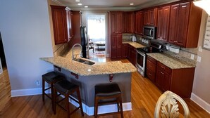 A modern kitchen with granite countertops, wooden cabinets, and a central island with bar stools. - Executive Home on over an Acre of Land.  Country Living at its Best. (Youngsville)