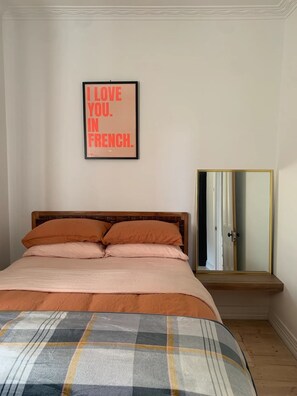 A bedroom with a bed, pillows, a plaid blanket, a mirror, and a framed sign on the wall. - Armstrong Cottage (Ballarat Central)