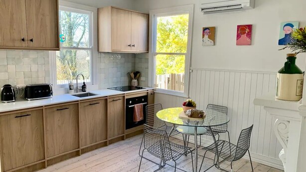 Une cuisine moderne avec des meubles en bois, un four encastré et un coin repas comprenant des chaises en métal et une table en verre.