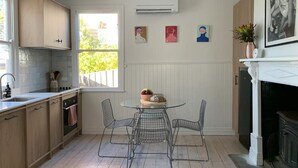 Une cuisine avec des meubles en bois, un plan de travail blanc, un évier, une table à manger avec des chaises en fil de fer et une cheminée.