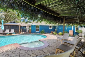 A swimming pool with lounge chairs, a covered patio, and a blue house in the background.