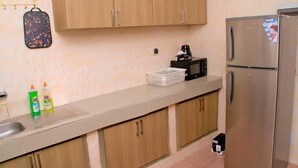 A kitchen with wooden cabinets, a stainless steel refrigerator, a coffee maker, and a basket on the counter. - Résidence Clean (Abidjan)