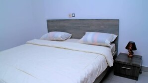 A neatly made bed with a wooden headboard, two pillows, and a bedside table with a lamp. - Résidence Clean (Abidjan)