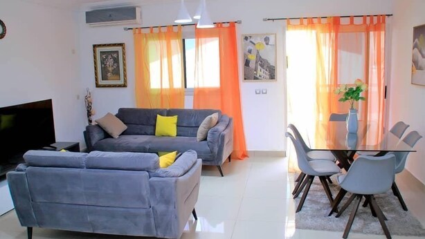A living room with a grey sofa, a TV, and a dining area with a glass table and chairs. - Résidence Clean (Abidjan)