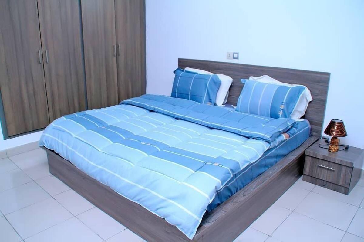 A bedroom with a large bed, wooden wardrobe, and a bedside table with a lamp.