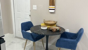 A dining area with a round table, two blue chairs, a wooden bowl, and a striped cloth hanging on the wall. - Beautiful Studio in Venice, Fl (Venice)
