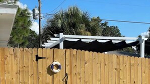 A wooden fence with a gate, a white structure with a roof, and a pathway leading to the gate. - Beautiful Studio in Venice, Fl (Venice)