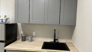 A kitchen with grey cabinets, a black sink, a coffee container, and a small appliance. - Beautiful Studio in Venice, Fl (Venice)
