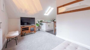 Un salon moderne avec un téléviseur à écran plat, un banc rembourré, une petite armoire en bois et une plante en pot.