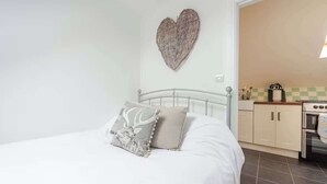 Une chambre avec un lit, une décoration murale en forme de cœur et, au fond, une petite cuisine.