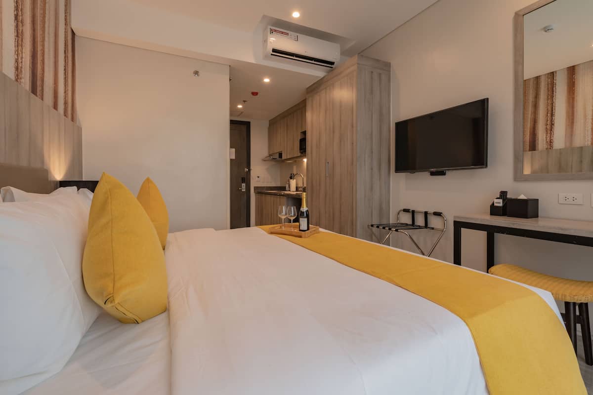 A hotel room with a bed, a bedside table, a TV, and a small kitchenette.