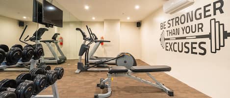 Un gimnasio con equipo de ejercicio, una frase motivacional en la pared y un extintor.