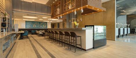 A modern bar area with a long counter and multiple stools, a ceiling with recessed lighting, and a decorative wall with circular patterns.