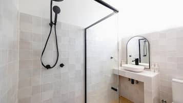 Un baño moderno con cabina de ducha de vidrio, un lavabo blanco con espejo y un inodoro.