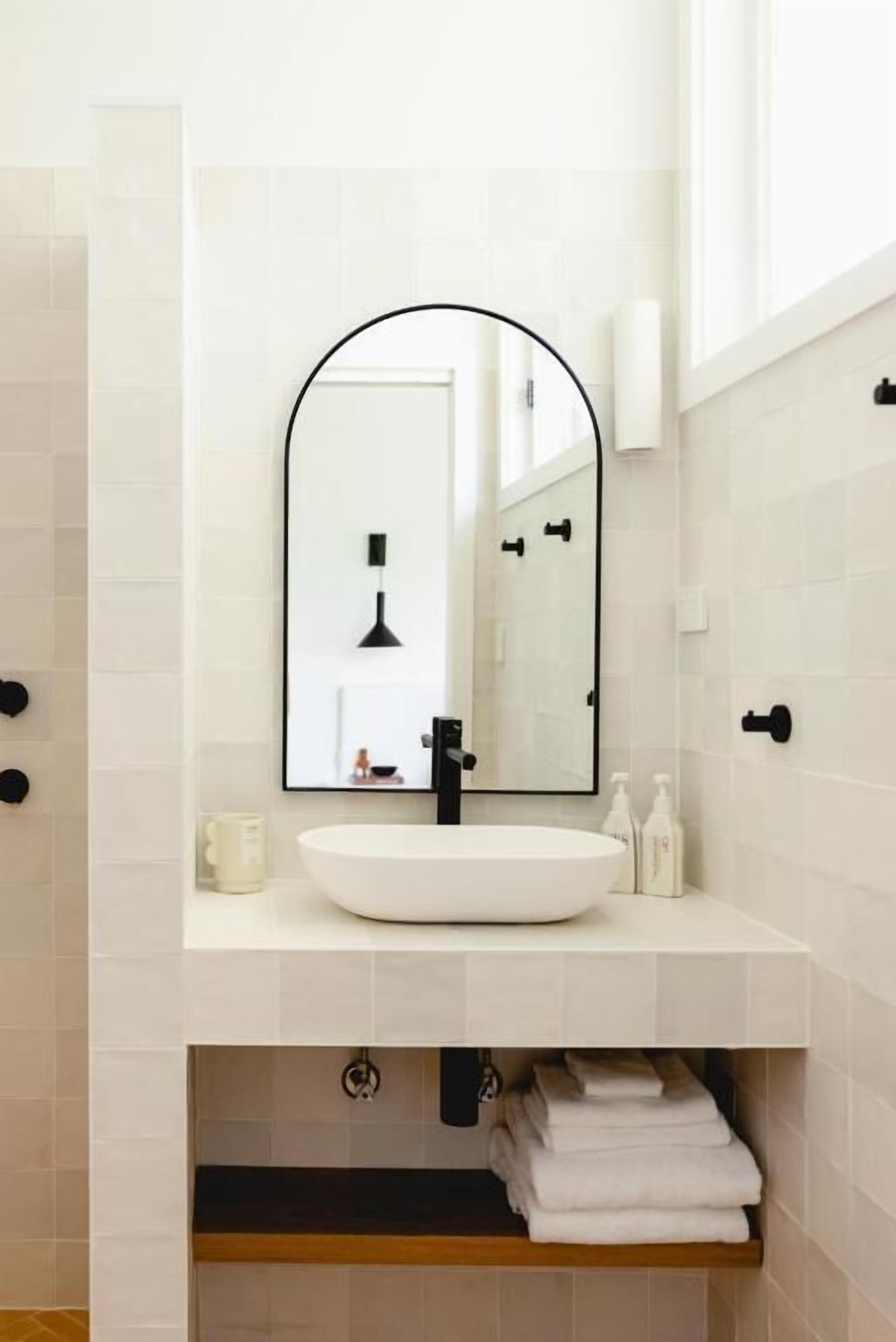 A modern bathroom with a white sink, a large mirror, and a towel rack.