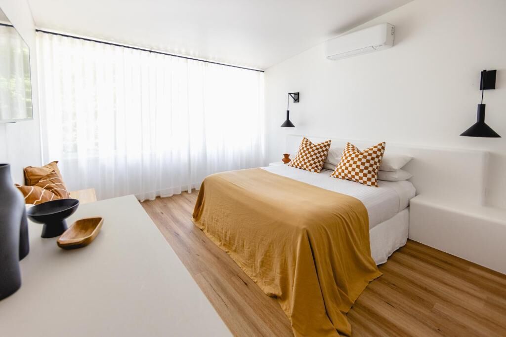 Une chambre moderne avec un grand lit, des murs blancs, un plancher en bois et une fenêtre ornée de rideaux légers.