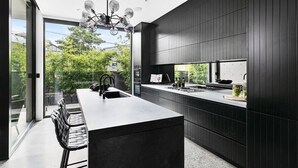 A modern kitchen with a central island, dark wood paneling, and a large window overlooking greenery.