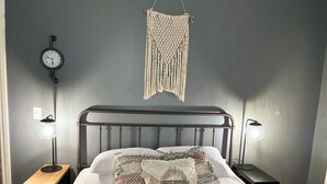Un dormitorio con una cama, dos lámparas de noche, un reloj de pared y un colgador de macramé.