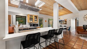 Cozinha moderna com ilha central, banquetas pretas e área de refeições com vista para a piscina.