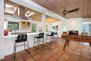 A modern kitchen with a bar area, a foosball table, and a dining area with chairs.