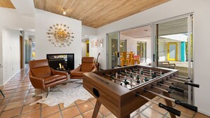 Uma sala de estar moderna com teto de madeira, mesa de futebol, poltronas de couro e lareira.