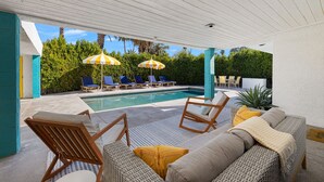 Área de piscina descoberta coberta, com espreguiçadeiras, guarda-sóis e um sofá de vime.