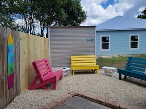Relax in a casual outdoor seating area with benches and a table, surrounded by a wooden fence and a surfboard decoration.