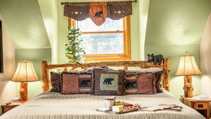 A bedroom with a bed, two bedside lamps, a window with a view, a small Christmas tree, and a bear-themed pillowcase.